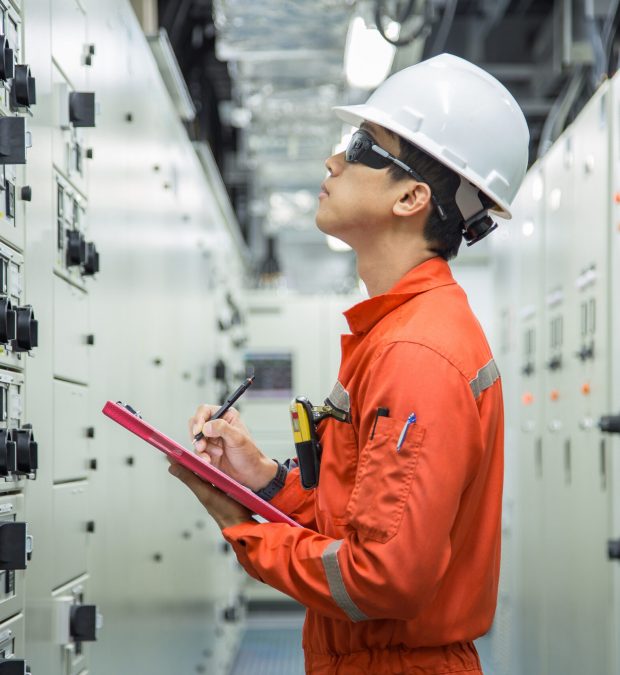 Electrician reading and recording the voltage current and power of electrical power distribution board in switch gear room for maintenance and performance monitor.