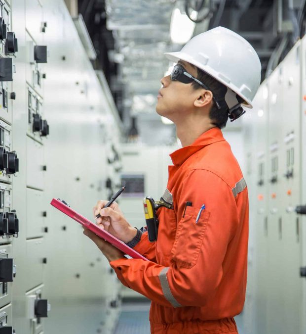 Electrician reading and recording the voltage current and power of electrical power distribution board in switch gear room for maintenance and performance monitor.