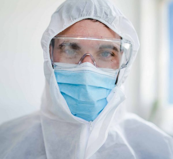 Front view portrait of young male caucasian doctor medic wearing protective suit eyeglasses and surgical mask at hospital - Safety protection paramedic during covid-19 pandemic - healthcare concept