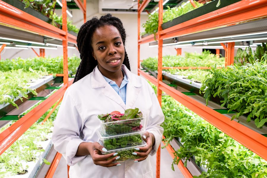 Cheerful young African greenhouse worker in whitecoat holding three containers
