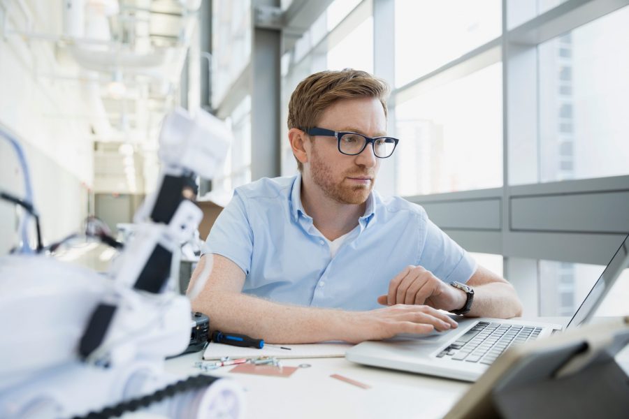 Focused engineer working at laptop next to robot